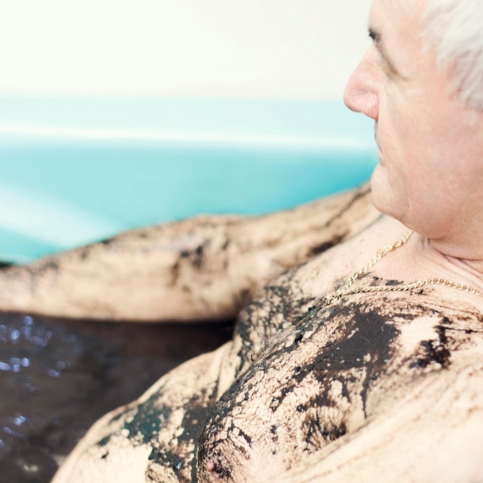 Kąpiel borowinowa - mężczyzna siedzi w wannie wypełnionej brązową zawiesiną borowinową. Klatkę piersiową pokrywa mu borowina.
