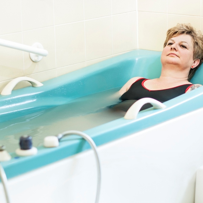 Kąpiel siarczkowa. Kobieta siedzi w turkusowej wannie wypełnionej leczniczą wodą siarczkową.